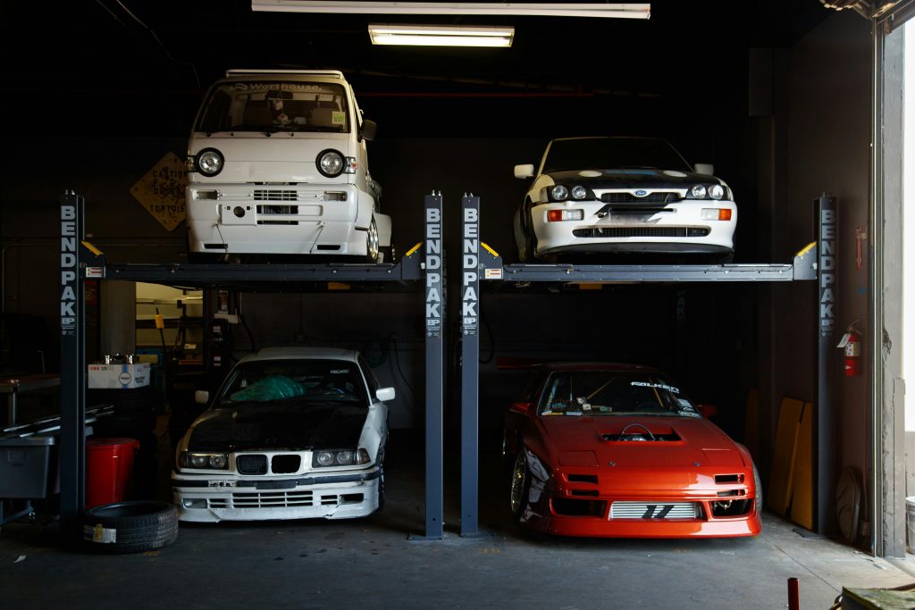 A collection of modified sports cars on a mechanical garage lift in Compton, CA.